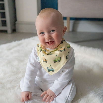 Baby wearing a white outfit and a yellow bib with green vehicle patterns