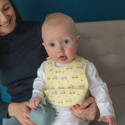 Baby wearing a yellow bib with vehicle patterns