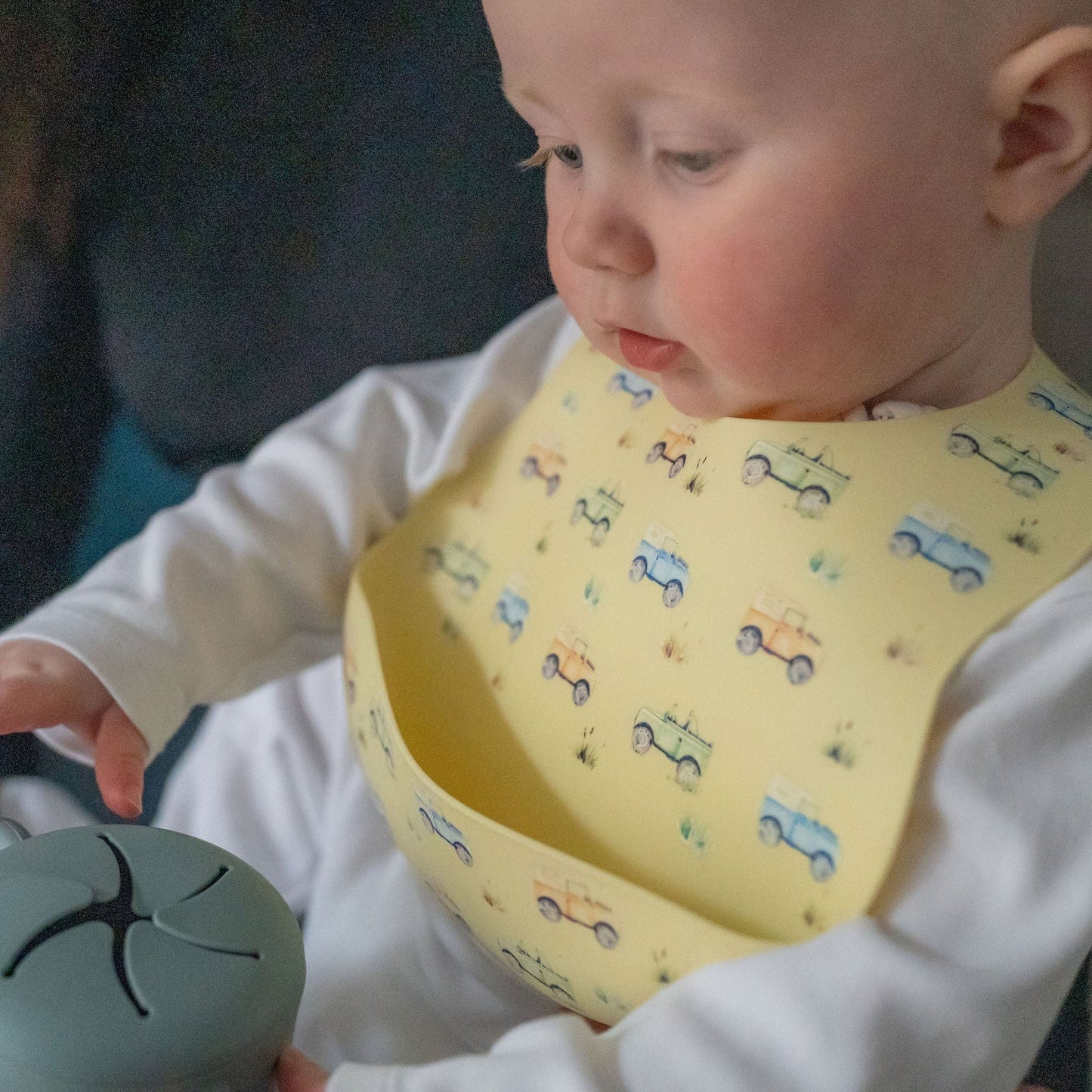 Baby wearing a yellow bib with car patterns