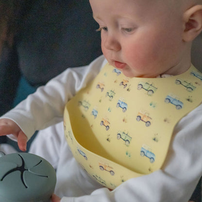 Baby wearing a yellow bib with car patterns