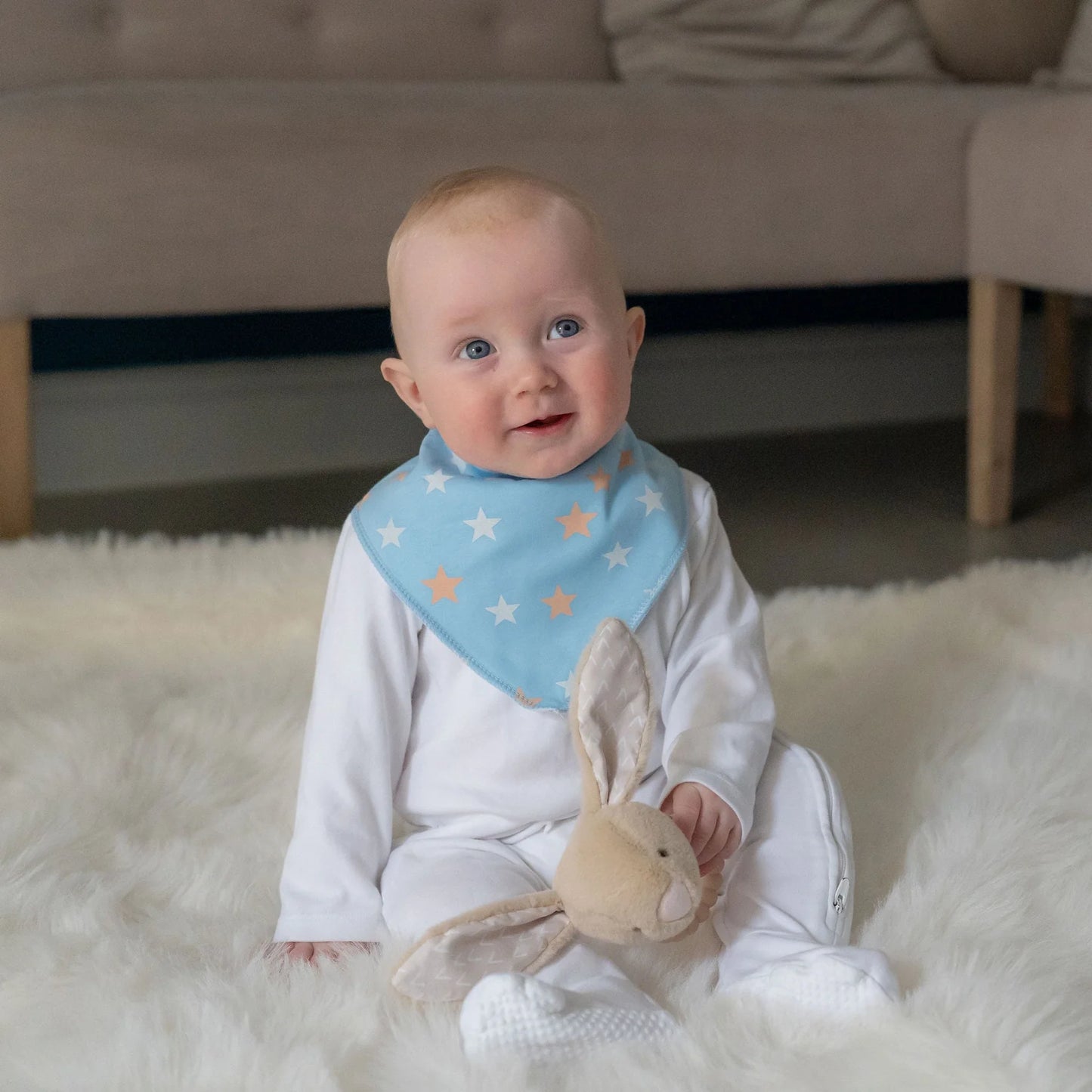 Baby wearing a blue bib with star pattern, holding a plush toy