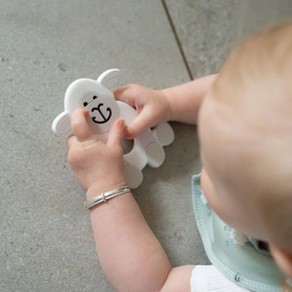 Baby playing with a white toy resembling a sheep on a gray floor.